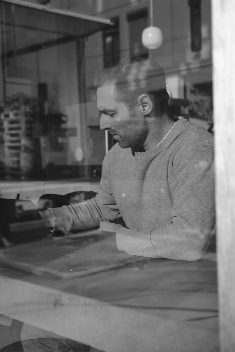 Philip Kerr working at a laptop, photographed through a window with urban reflections
